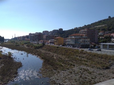 Stazione di Imperia. Torrente Impero e Via Argine Destro. La stazione ha due ingressi, uniti dalle banchine dei binari o da un ponte che unisce i due fabbricati viaggiatori siti in Via Argine Sinistro e Via Argine Destro.